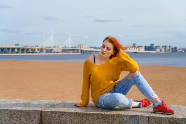 Atrakcyjna młoda ruda kobieta siedzi na zewnątrz na nabrzeżu w kolorze żółtym