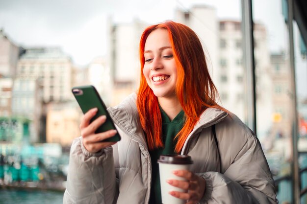 Atrakcyjna młoda rudowłosa kobieta wpisuje wiadomość przez telefon komórkowy na promie w Stambule i się uśmiecha