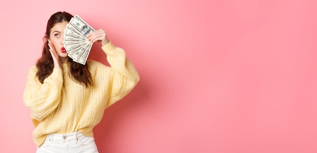 Atrakcyjna modelka pokazująca pieniądze trzymające banknoty dolarowe na połowie twarzy dotykająca policzka i robiąca