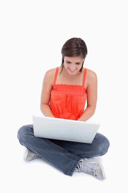 Atrakcyjna nastolatka siedzi ze skrzyżowanymi nogami pisania na laptopa