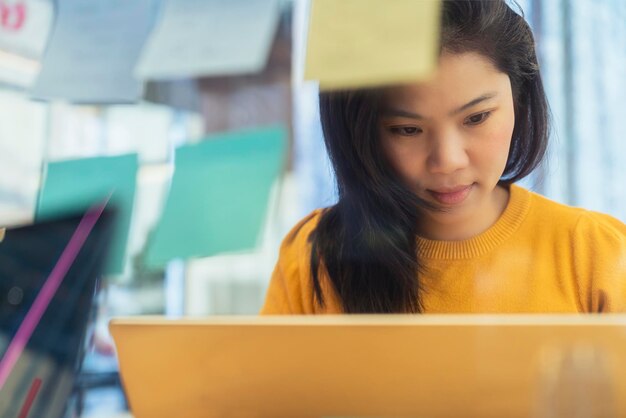 Atrakcyjna niezależna azjatycka kobieta kreatywna nosi na co dzień żółty materiał do pracy z laptopem w obszarze współdzielenia przestrzeni coworkingowej nowy styl życia z przemyślanym i świeżością rozmycie emocji w tle biurowym
