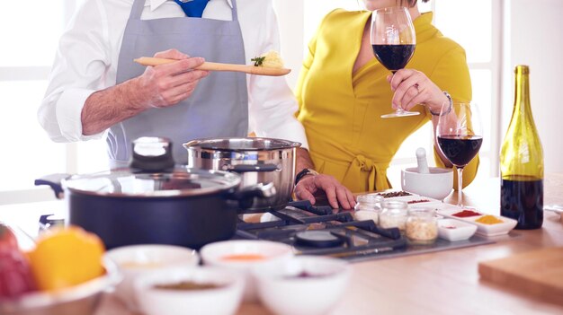 Atrakcyjna para zakochana w gotowaniu i otwieraniu wina w kuchni podczas gotowania kolacji na romantyczny wieczór