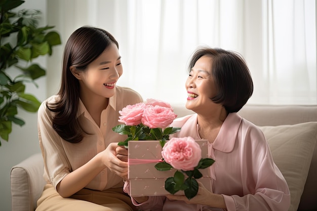 Atrakcyjna piękna azjatycka matka w średnim wieku siedzi z dorosłą córką daje pudełko z prezentami i kwiaty w rodzinie