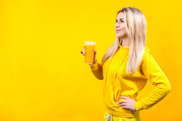Atrakcyjna piękna młoda blondynki kobieta w żółtym przypadkowym sportowym ubraniu trzyma szkło soku pomarańczowego