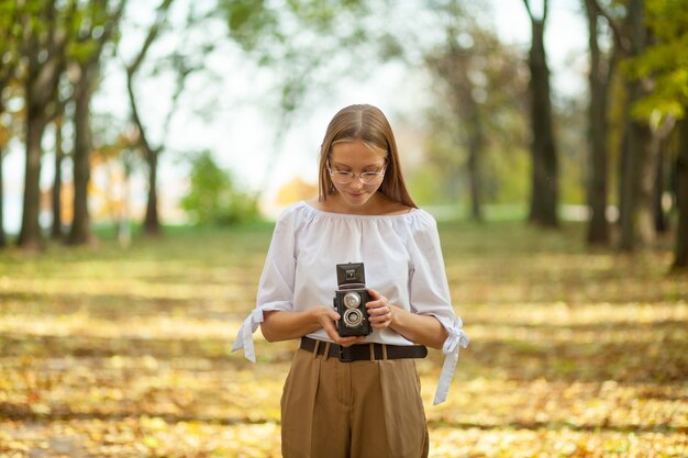 Atrakcyjna, piękna, młoda dziewczyna trzyma aparat odbicie retro starodawny podwójny obiektyw w parku jesienią