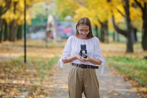Atrakcyjna, piękna, młoda dziewczyna trzyma aparat odbicie retro starodawny podwójny obiektyw w parku jesienią