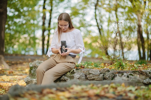 Zdjęcie atrakcyjna, piękna, młoda dziewczyna trzyma aparat odbicie retro starodawny podwójny obiektyw w parku jesienią
