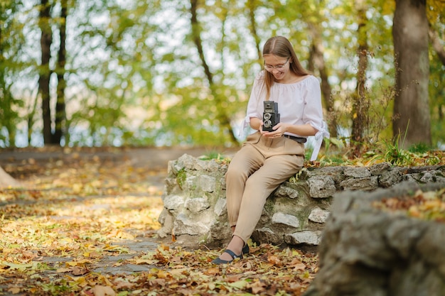 Atrakcyjna, piękna, młoda dziewczyna trzyma aparat odbicie retro starodawny podwójny obiektyw w parku jesienią