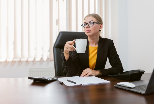 Atrakcyjna Szefowa Pije Kawę W Swoim Biurze, Siedząc Przy Stole Z Laptopami