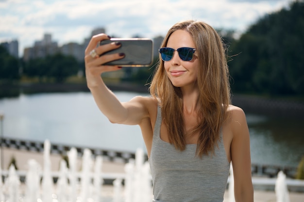 Atrakcyjna turystyczna dziewczyna robi selfie z brzeg rzeki na tle w miasto parku