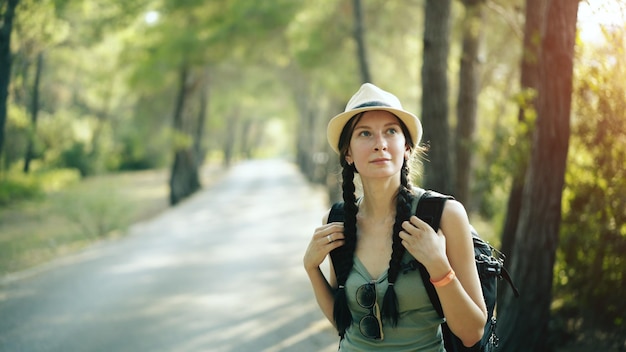 Atrakcyjna turystyczna dziewczyna uśmiecha się i patrzy w kamerę podczas spaceru i wędrówki po pięknym lesie