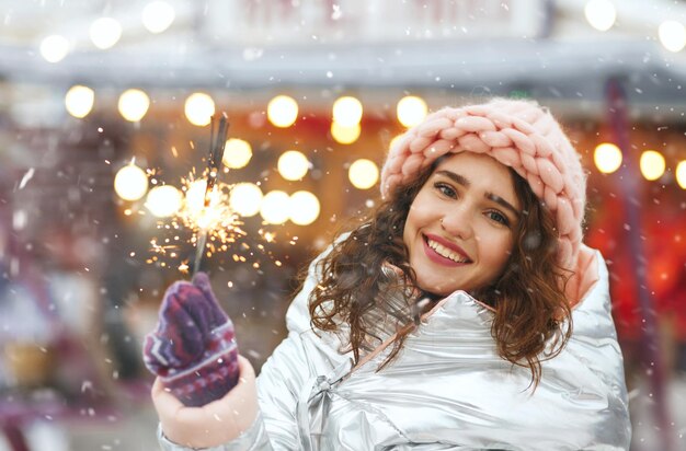 Atrakcyjna uśmiechnięta kobieta bawi się musujące światła na jarmarku bożonarodzeniowym. Pusta przestrzeń