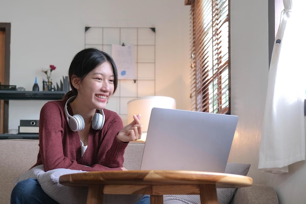 Atrakcyjna uśmiechnięta młoda kobieta wideorozmowa przez laptopa na kanapie w koncepcji stylu życia w domu