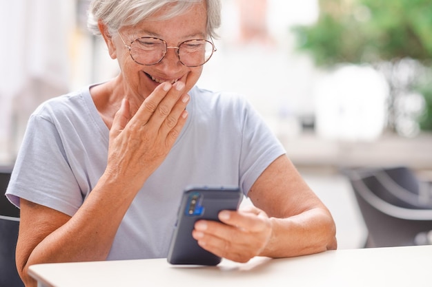 Atrakcyjna uśmiechnięta starsza kobieta korzystająca z telefonu siedząca przy barze starsza pani śmiejąca się na czacie wideo
