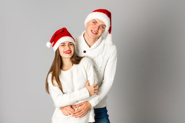 Atrakcyjna zakochana para świętuje Boże Narodzenie i bawi się w santa hats w studio na szarym tle