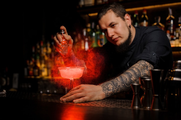 Atrakcyjny barman spryskujący pyszny koktajl ze specjalnego waporyzatora na blacie barowym