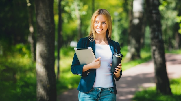 Atrakcyjny biznes dziewczyna za pomocą tabletu, pijąc kawę w parku