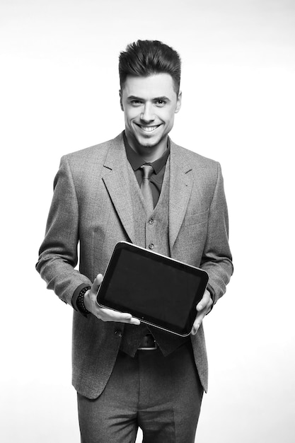 Atrakcyjny biznesmen uśmiechający się i trzymający swój tablet, mając na sobie czerwony krawat i niebieski garnitur stojący na białym tle studia