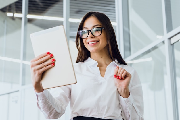 Zdjęcie atrakcyjny bizneswoman używa cyfrową pastylkę podczas gdy stojący w wielkim korporacyjnym budynku