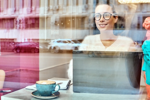 Atrakcyjny Bizneswoman W Okulary Optyczne Obile Rozmowa Z Przyjacielem Za Pomocą Smartfona. Pozytywna Młoda Kobieta Rozmawia Przez Telefon, Siedząc Przy Komputerze W Kawiarni