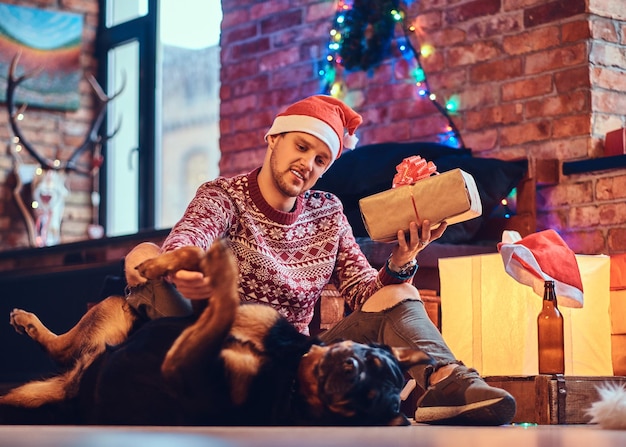 Atrakcyjny brodaty samiec hipster z psem Rottweiler w pokoju ze świąteczną dekoracją.