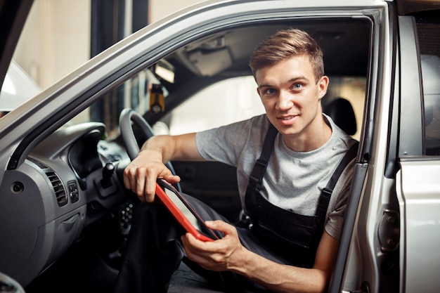 Atrakcyjny i dobrze wyglądający mechanik samochodowy sprawdza samochód podczas pracy.