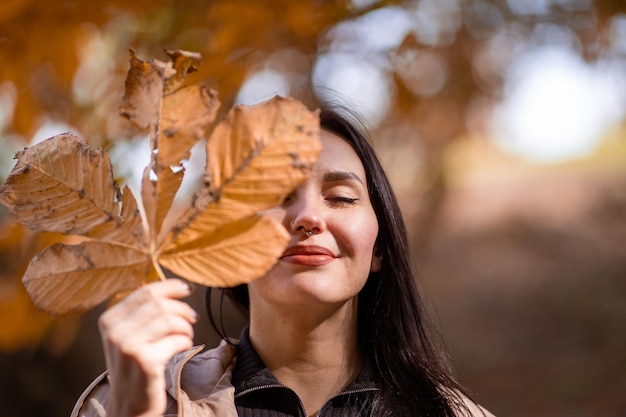 Atrakcyjny i stylowy portret kobiety w sezonie jesiennym pozuje z żółtym liściem