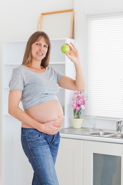 Atrakcyjny kobieta w ciąży pozuje podczas gdy trzymający zielonego jabłka