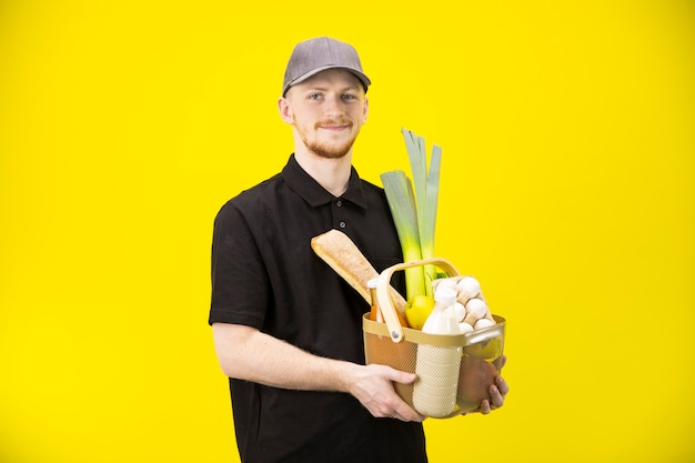 Atrakcyjny męski kurier trzyma kosz z produktami rolnymi, zakupy spożywcze online
