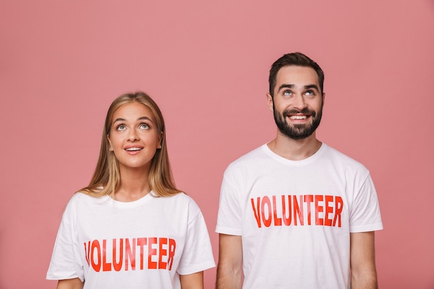 atrakcyjny mężczyzna i kobieta ochotnicy noszący jednolite koszulki, patrzący w górę na copyspace na białym tle