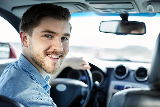 Atrakcyjny mężczyzna siedzi w samochodzie i patrząc na kamery i uśmiechnięty, kupując nowy samochód.