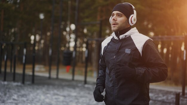 Atrakcyjny mężczyzna w słuchawkach robi ćwiczenie rozgrzewkowe przygotowujące do biegania podczas słuchania muzyki