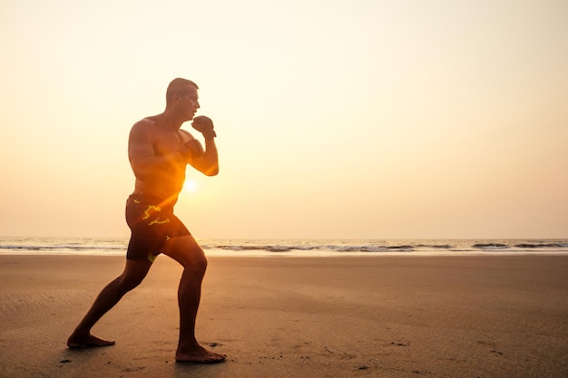 Atrakcyjny mężczyzna z nagim torsem podczas treningu na plaży sportowy model mężczyzna robi trening fitness na plaży w słoneczny wieczór o zachodzie słońca