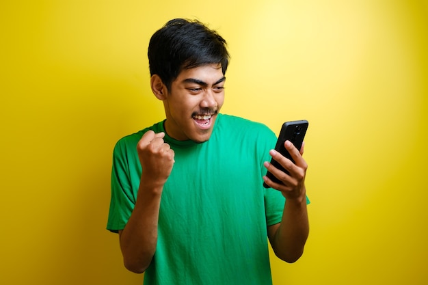 Atrakcyjny młody Azjata ma dobre wieści na swoim telefonie, uśmiechając się, śmiejąc się, śmiejąc się, wygrywając na żółtym tle
