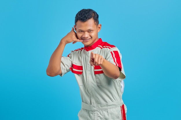 Atrakcyjny młody azjatycki mechanik robiący znak gestu wywołania i wskazujący na kamerę na niebieskim tle