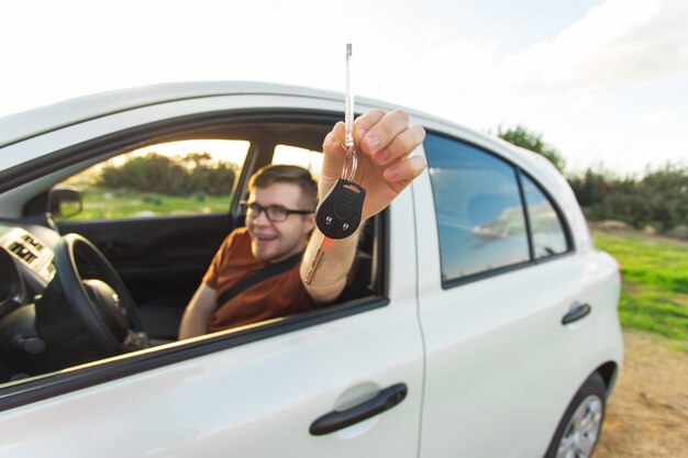 Atrakcyjny młody człowiek szczęśliwy pokazując swoje nowe kluczyki do samochodu i śmiejąc się.