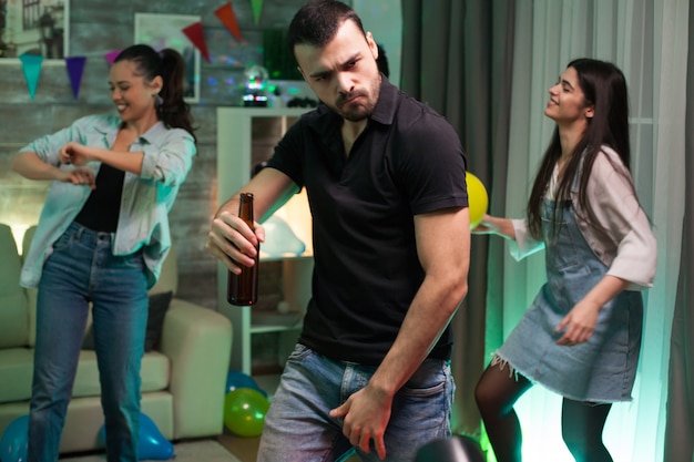 Atrakcyjny młody człowiek z butelką piwa w ręku tańczy na imprezie z przyjaciółmi. Dziewczyna z balonem.