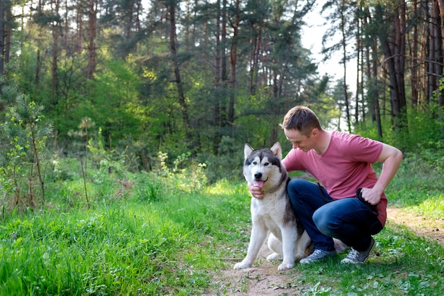 Atrakcyjny młody człowiek z psem malamute na spacerze w lesie