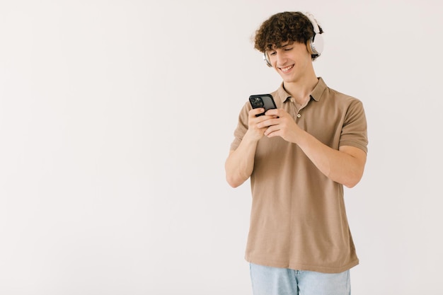 Atrakcyjny młody student płci męskiej w nowoczesnych słuchawkach za pomocą telefonu na białym tle z wolną przestrzenią