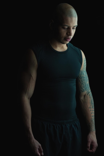 Atrakcyjny muskularny młody człowiek w ciemnych ubraniach na ciemnym tle wyglądający na zamyślony