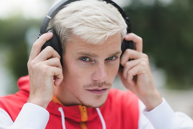 Atrakcyjny portret nowoczesnego blondyna w czerwonej odzieży sportowej i słuchawkach do słuchania muzyki w parku na świeżym powietrzu Młody przystojny mężczyzna słucha muzyki w słuchawkach na świeżym powietrzu