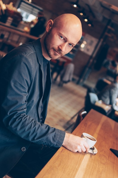 Atrakcyjny poważny łysy mężczyzna z kawą patrzeje kamerę w kawiarni