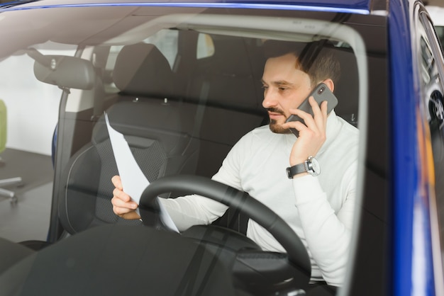 Atrakcyjny przystojny młody biznesmen za pomocą inteligentnego telefonu komórkowego w samochodzie.