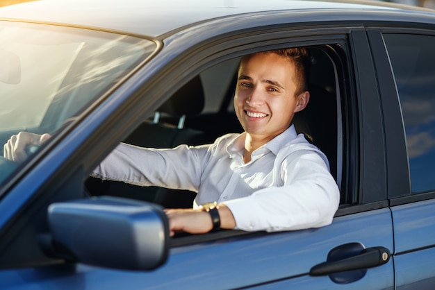 Atrakcyjny przystojny uśmiechnięty mężczyzna w białej koszuli jazdy drogim samochodem
