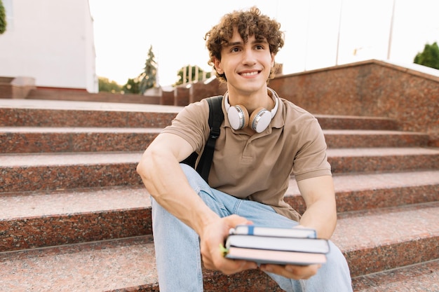 Zdjęcie atrakcyjny student siada na stopniach uczelni i czyta coś przygotowując do egzaminów