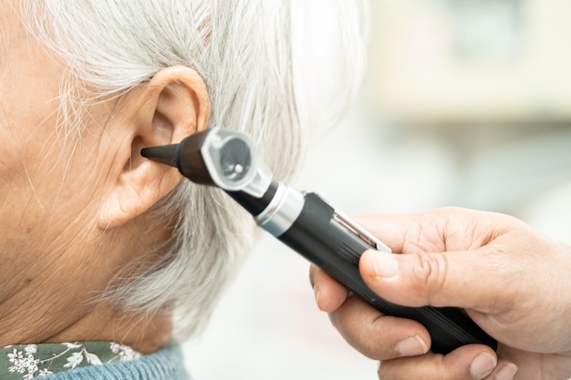 Audiolog lub lekarz laryngolog używa otoskopu sprawdzającego ucho azjatyckiej starszej pacjentki