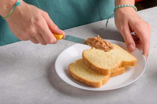 Autentyczne ręce kobiet rozciągające masło orzechowe na kawałku białego toastu