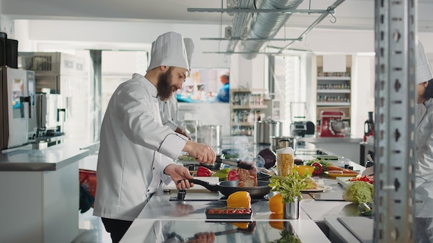 Autentyczny Szef Kuchni Gotuje Stek Mięsny Na Patelni Na Kuchence, Używając Przyborów Kuchennych I Smacznych Składników. Mężczyzna Kucharz Przygotowuje Posiłek Z Kulinarnym Przepisem Na Dania Z Menu Restauracji.