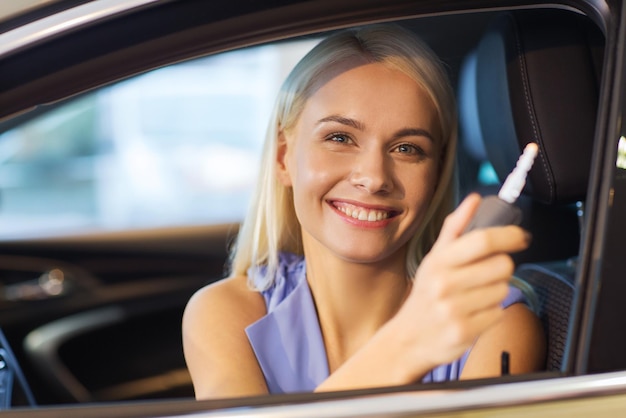 auto biznes, sprzedaż samochodów, konsumpcjonizm i ludzie pojęcie - szczęśliwa kobieta bierze klucz samochodowy od sprzedawcy w auto przedstawieniu lub salonie