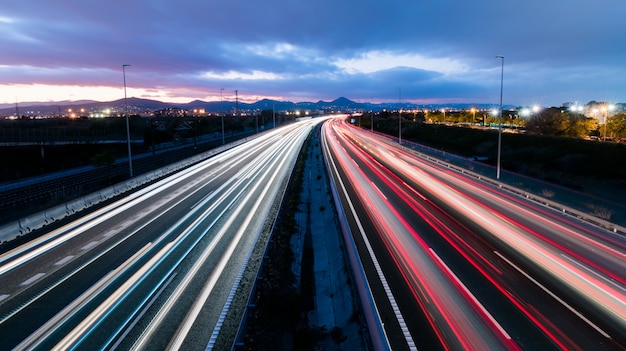 Autostrada O Zachodzie Słońca Z Pojazdami Jadącymi W Dwóch Kierunkach, Pozostawiając Smugi światła